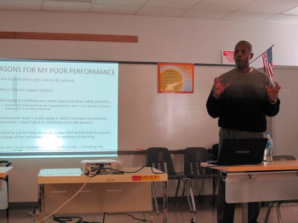 A man standing in front of a projector screen.